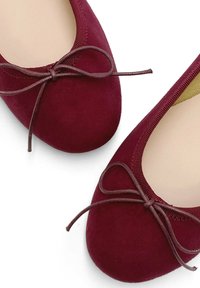 Ballerines en daim bourgogne avec un bout rond, un délicat nœud marron, et une surface douce et texturée. Doublure intérieure lisse en beige.
