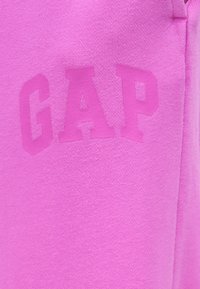 Φωτεινό ροζ ύφασμα με κεντημένο το λογότυπο GAP σε μεγάλες, έντονες γράμματα, κεντραρισμένο στο υλικό.