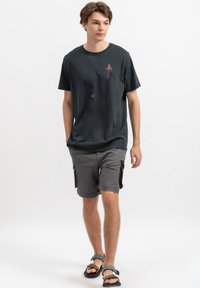 Zwart katoenen T-shirt met een kleine kleurrijke afbeelding op de borst, gecombineerd met grijze cargoshorts en zwarte slippers. Slim fit ontwerp.