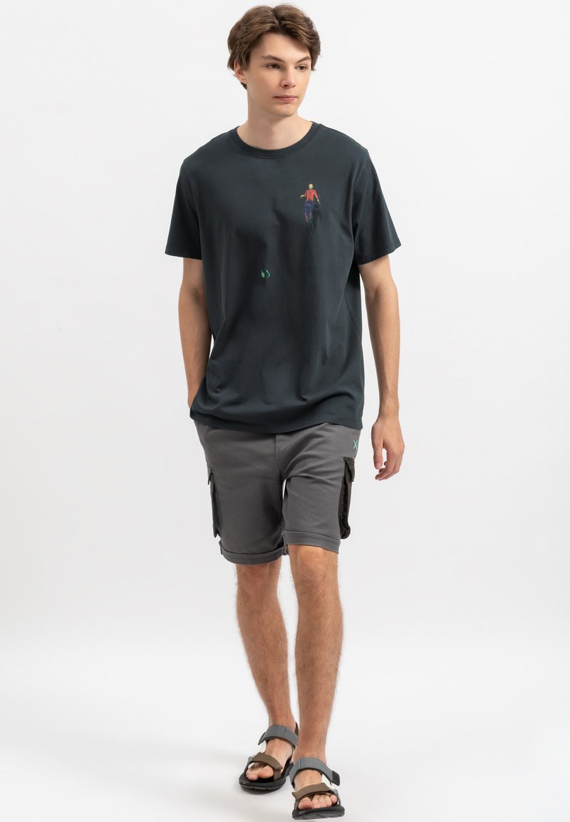 Zwart katoenen T-shirt met een kleine kleurrijke afbeelding op de borst, gecombineerd met grijze cargoshorts en zwarte slippers. Slim fit ontwerp.