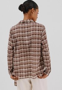 Bruine geruite blouse met lange mouwen, een klassieke kraag en een ontspannen pasvorm. De stof heeft een gladde textuur met een gemengd patroon.