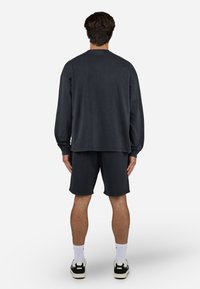 Maglietta a maniche lunghe grigio scuro abbinata a pantaloni corti coordinati; materiale in cotone, vestibilità comoda e dettaglio dell'orlo arrotondato. Calzini bianchi e calzature nere.