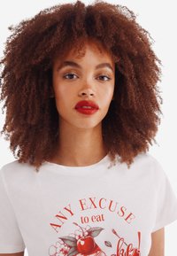 Hvid bomulds T-shirt med rød grafisk tekst og frugtbilleder. Korte ærmer og rund halsudskæring, med en glat tekstur.