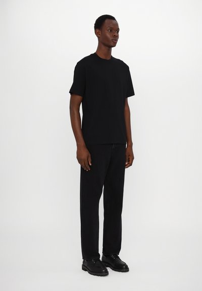 Tricou din bumbac negru cu mâneci scurte, guler rotund și o croială lejeră, asortat cu pantaloni negri drepti și pantofi negri cu șiret.