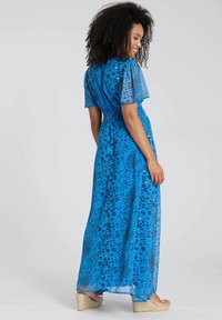 Maxikleid aus blauer, transparenter Stoff mit einem Leopardenmuster. Es hat kurze Puffärmel und eine geraffte Taille, die für eine fließende Silhouette sorgt.