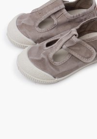 Hellbraune Leinenschuhe mit elastischen Riemen, runden weißen Gummispitzen und strukturierten Sohlen. Mit seitlichen Ausschnitten.