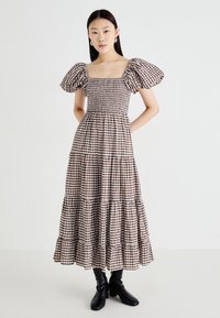 Bruin en crème geruit katoenen jurk met pofmouwen, getailleerde top en gelaagde rok. Draag met zwarte enkellaarsjes.