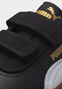 Μαύρο αθλητικό παπούτσι με δύο ιμάντες Velcro, λευκή πλαϊνή επιφάνεια και χρυσό λογότυπο Puma στη γλώσσα και στο πλάι.