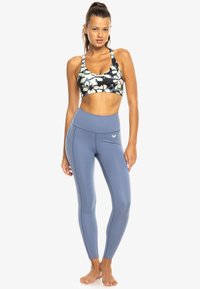 Soutien-gorge de sport athlétique avec un motif floral bleu marine et blanc, associé à des leggings taille haute et ajustés de couleur bleu clair.