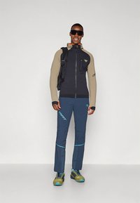 Manns utendørsantrekk med en mørkegrå og beige jakke, blå bukser med lyseblå detaljer, og vanntette tursko.