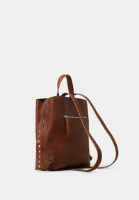 Zaino in pelle marrone con una forma strutturata, dotato di una tasca con zip frontale, spallacci lunghi e borchie decorative in argento sui lati.