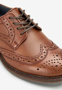 Chaussure habillée en cuir marron avec des détails en brogue perforés, des lacets ronds et une surface texturée avec une finition lisse.