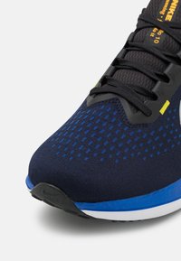 Scarpa da atletica blu e nera con tomaia in rete, motivo testurizzato, lacci piatti e suola imbottita con accenti bianchi e blu.