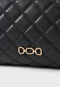 Μαύρη καπιτονέ δερμάτινη τσάντα με διακοσμητική χρυσή αλυσίδα. Η επιφάνεια έχει υφή με έντονες λεπτομέρειες ραφής.