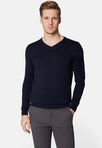 Ciemnoniebieski sweter w serek z długimi rękawami, z ribbami na mankietach i dole, wykonany z miękkiego materiału dzianinowego. Posiada małe logo na piersi.