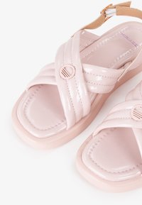 Sandali in plastica patent rosa con fasce incrociate e dettaglio a bottone. Suola morbida con punta squadrata e soletta imbottita.