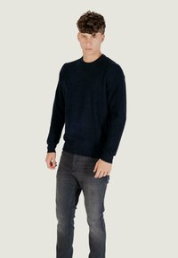 Mornarsko plava rebrasta pletena bluza s okruglim izrezom i dugim rukavima, u kombinaciji s tamnosivim uskim trapericama. Sveukupni teksturirani izgled.