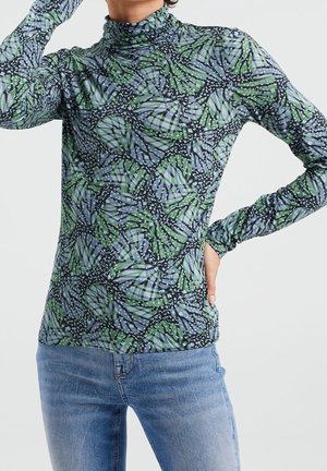 Strakvallend top met lange mouwen, bedrukt met een abstract bladpatroon in groen, blauw en zwart, gecombineerd met een blauwe spijkerbroek.