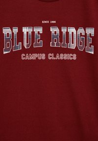 Bordo spalvos džemperis su baltu tekstu: "BLUE RIDGE" su kilpiniais raštais. Papildomas tekstas skelbia "CAMPUS CLASSICS" ir "SINCE 1986." Lygus paviršius.