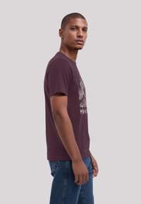 Maroon cotton t-shirt with a crew neck, short sleeves, and a graphic design featuring intricate detail and stylized text on the front.