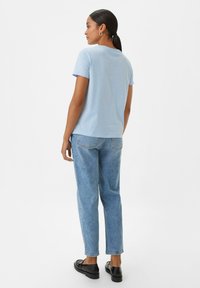 Lichtblauwe t-shirt met korte mouwen, voorzien van een ronde halslijn en een comfortabele pasvorm, gecombineerd met hoogopgestoken lichtblauwe denim jeans en zwarte schoenen.