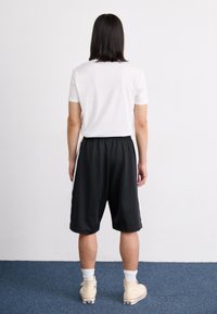 Sorte atletiske shorts med elastisk talje, parret med en hvid t-shirt. Kort længde, glat tekstur og bæres med høje sneakers.