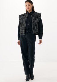 Černý tvídový vest s pevným designem, který má vysoký výstřih a široké průramky. Doplňuje s vysokým pasem černými džíny a lodičkami.