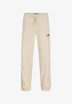 Pantalones de chándal beige hechos de tela suave, con cinturilla elástica, cordón ajustable y detalle del logo negro en la cadera. Dobladillos ajustados.