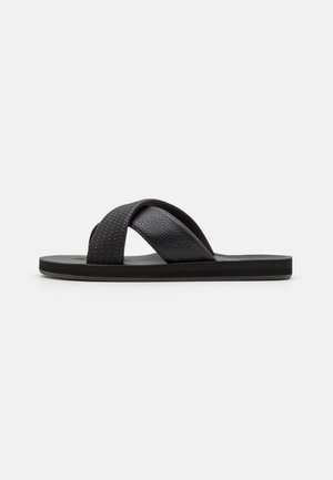 Black sandals with a textured cross-strap design and flat sole. Made of synthetic materials, featuring a smooth finish and subtle branding.