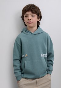 Turquoise hoodie met een voorzak, voorzien van grafische accenten in wit en oranje. Zachte stof, ontspannen pasvorm en een capuchon met trekkoord.