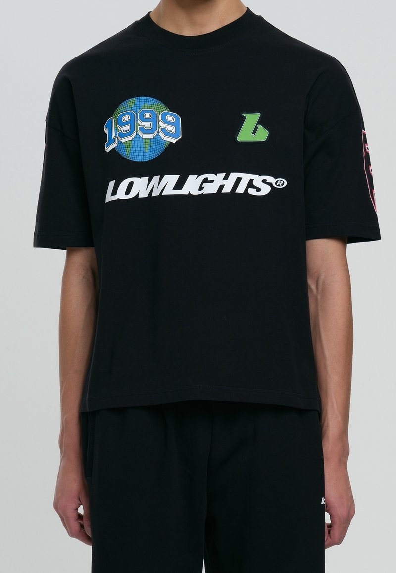 T-shirt noir à manches courtes présentant un graphique de globe, "1999," et "LOWLIGHTS" en gras blanc, avec une coupe allongée et un design détendu.