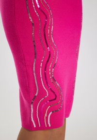 Rochie tricotată fuchsia cu modele de valuri din paiete strălucitoare în argintiu și roz, având o siluetă ajustată și o margine la mijlocul coapsei.