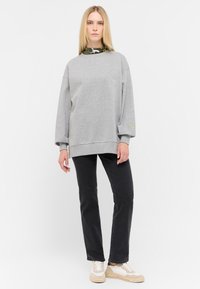 Sudadera gris de gran tamaño con mangas largas, con puños y dobladillo de canalé. Combinada con pantalones negros y zapatillas de color claro.
