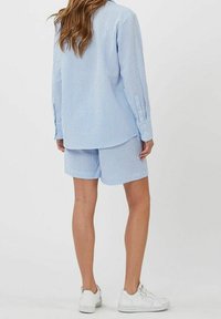 Chemise à rayures bleu clair à boutons et short assorti, avec une coupe décontractée et des baskets blanches, mettant en valeur une texture douce de coton.