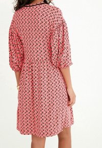 Robe rose à motifs, ornée de motifs floraux noirs, avec des manches courtes bouffantes, un col rond et une jupe évasée. Texture de tissu lisse.