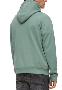 Muntgroene hoodie van zachte stof. Voorzien van een trekkoordkap, ribgebreide manchetten en zoom, en een relaxte pasvorm, gedragen met donkere jeans.