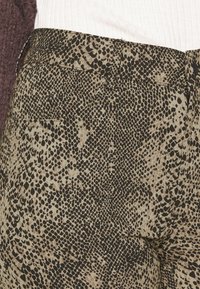 Skräddarsydda byxor i ormtryck, med textil med struktur i svart och beige färgskala, kombinerad midjedetalj och sidfickor.