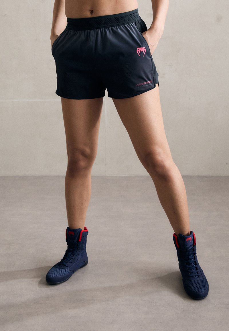 Schwarze Sportshorts mit einem rosa Logo und Seitentaschen, kombiniert mit navyblauen High-Top-Sneakers mit roten Akzenten und einem strukturierten Design.