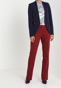 Blazer azul marino con un corte entallado y dos bolsillos laterales, combinado con una blusa en estampado de cebra en blanco y negro y pantalones rojos. Tacones negros completan el conjunto.