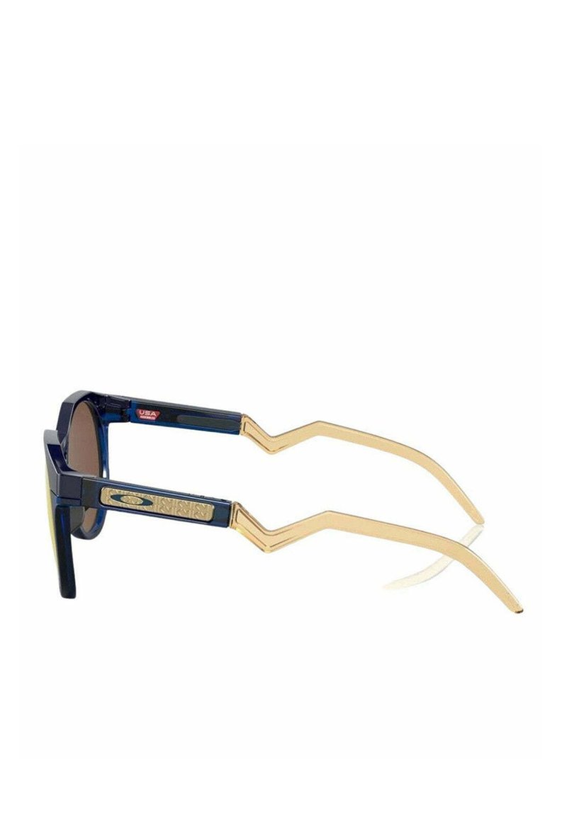 Lunettes de soleil avec une monture bleu marine, des accents dorés et un design d'armature en zigzag. Les verres sont teintés de marron avec une finition réfléchissante.