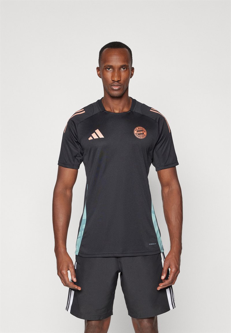 Sort træningsshirt med korte ærmer og turkise sidepaneler, orange logo og tre orange striber på skuldrene; parret med mørke shorts.