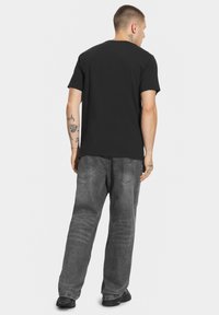 Czarna bawe łniana koszulka z okrągłym dekoltem, noszona z szarymi, luźnymi dżinsami o zblakłej teksturze i podwójnie szytymi szwami.