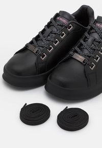 Schwarze Sneaker aus glattem synthetischem Material mit runden Zehen, Schnürdesign und pinker Markenbezeichnung. Inklusive schwarzer Schnürsenkel.