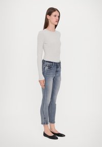 Világosszürke hosszú ujjú bordás felső, sötétkék, elhalványult hatású, slim fit farmernadrággal és fekete lapos cipővel párosítva.