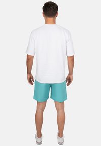 Outfit da uomo che include una maglietta bianca a maniche corte e pantaloni corti turchesi, abbinati a scarpe da ginnastica bianche. Design semplice, vestibilità casual e tessuto leggero.