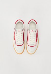 Hvite sneakers med røde detaljer, med en glatt læroverdel, perforert design og såle i gummi. Strikkene er hvite.