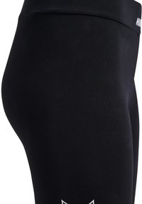 Gros plan sur des leggings noirs ajustés avec une taille élastique présentant un logo blanc partiel "HUMMEL" sur le côté.
