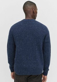 Tummansininen neulepusero, jossa on teksturoitu pinta, pyöreä kaula-aukko ja ribattu hihansuu ja helma. Sisältää roskatekstuurin kauttaaltaan.