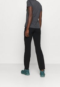 Harmaa lyhythihainen paita, mustat kapealahkeiset housut ja sinivihreät jalkineet. Sileä kangas ja hillitty muotoilu ilman kuvioita tai koristeita.