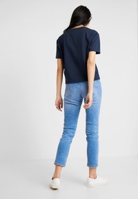 Navy tričko s krátkým rukávem a kulatým výstřihem, zkombinované s světle modrými skinny jeans a bílými teniskami, pohled zezadu.